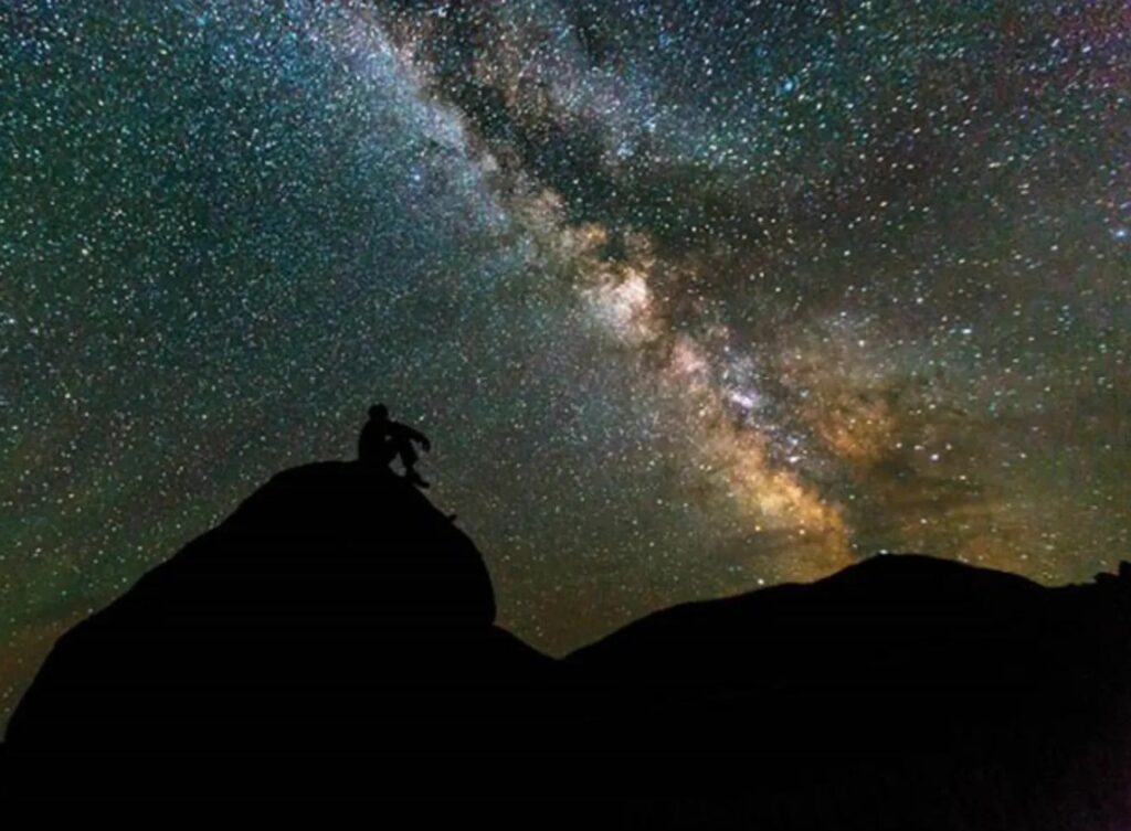 Person on hilltop, silhouetted by starry sky.