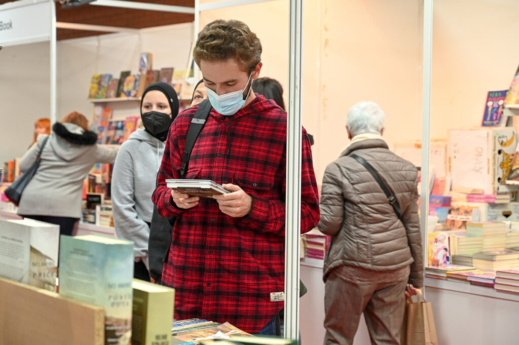 Young man wearing mask reading back cover of book in bookstore.