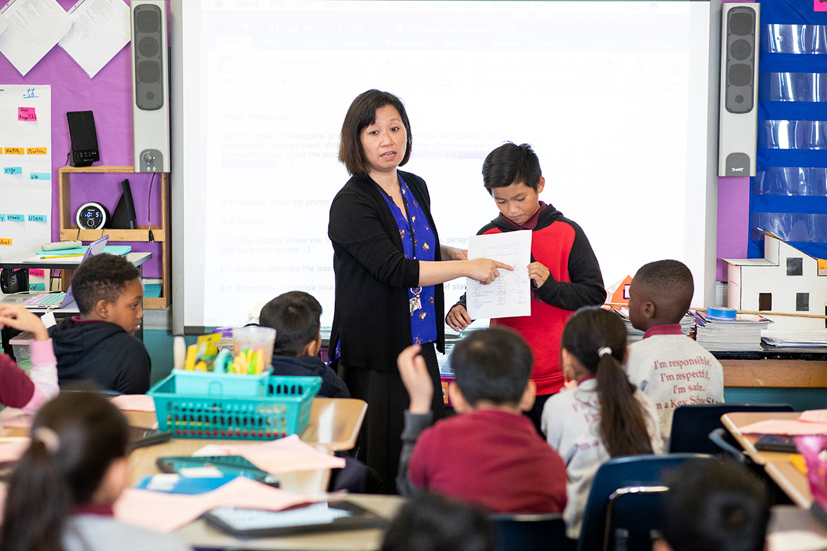 teacher pointing out student writing with student in front of class